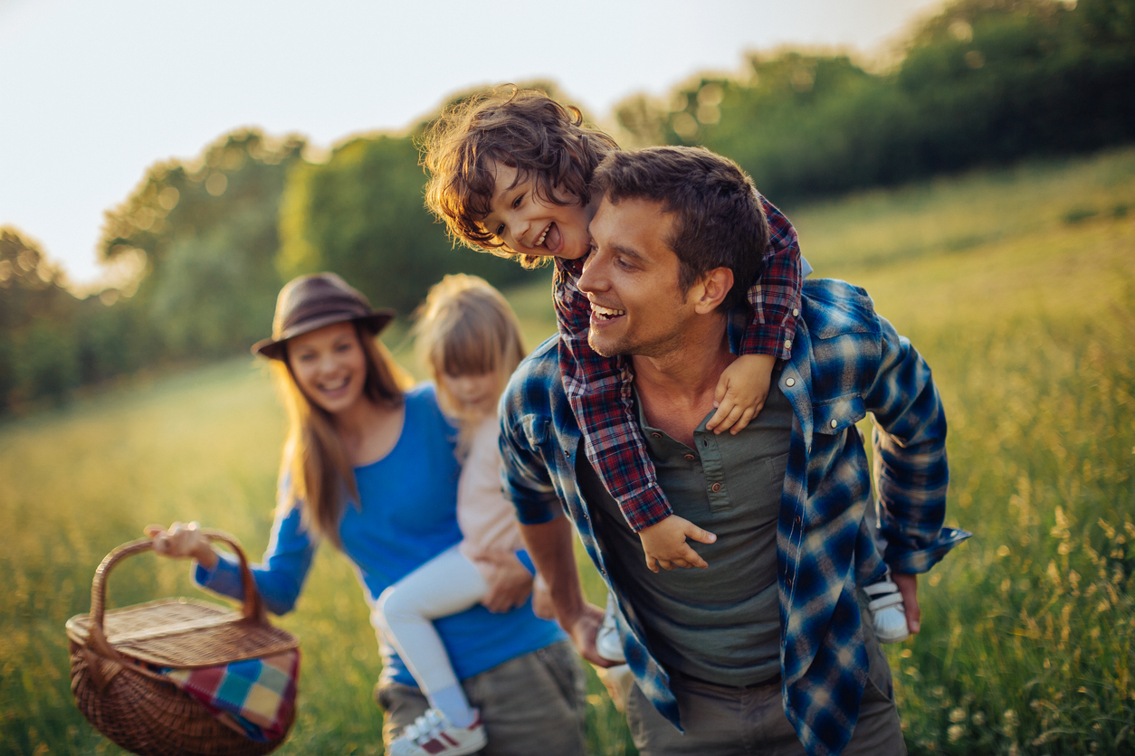 Picture of a young family going for a picnic, walking together threw high grass with the sun in their back.